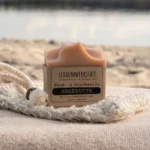 rosa Seife Hagebutte mit Banderole aus Kraftpapier steht auf einem Sisalsäckchen am Strand