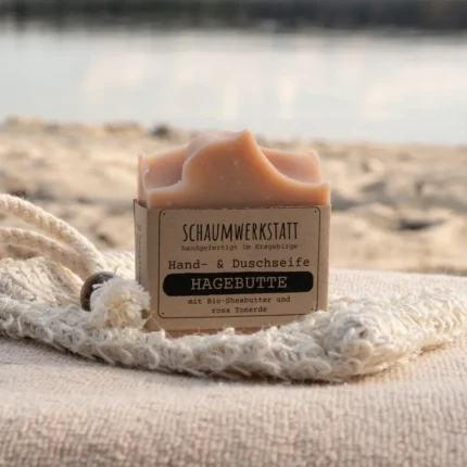 rosa Seife Hagebutte mit Banderole aus Kraftpapier steht auf einem Sisalsäckchen am Strand
