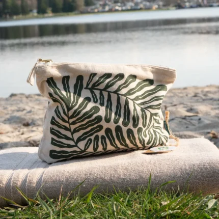 Kosmetiktasche aus Stoff mit dunkelgrünem Rankenprint auf einem Handtusch arrangiert.
