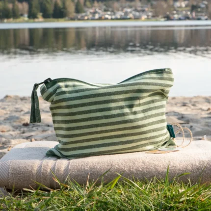 grün gestreifte Kosmetiktasche aus Stoff mit Reisverschluss auf einem Handtusch am Strand arrangiert