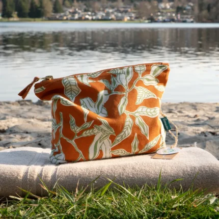 Orange Kosmetiktasche mit Lilien-Muster auf einem Handtuch arrangiert.