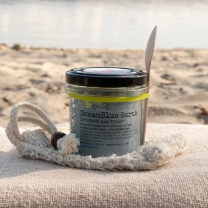 blaues Salzpeeling mit Meeresluft im Glas mit Holzlöffel am Strand arrangiert