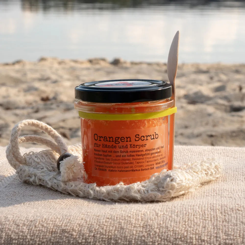 Peeling Orange Salzpeeling Orange im Glas mit Holzlöffel am Wasser auf Strandtuch