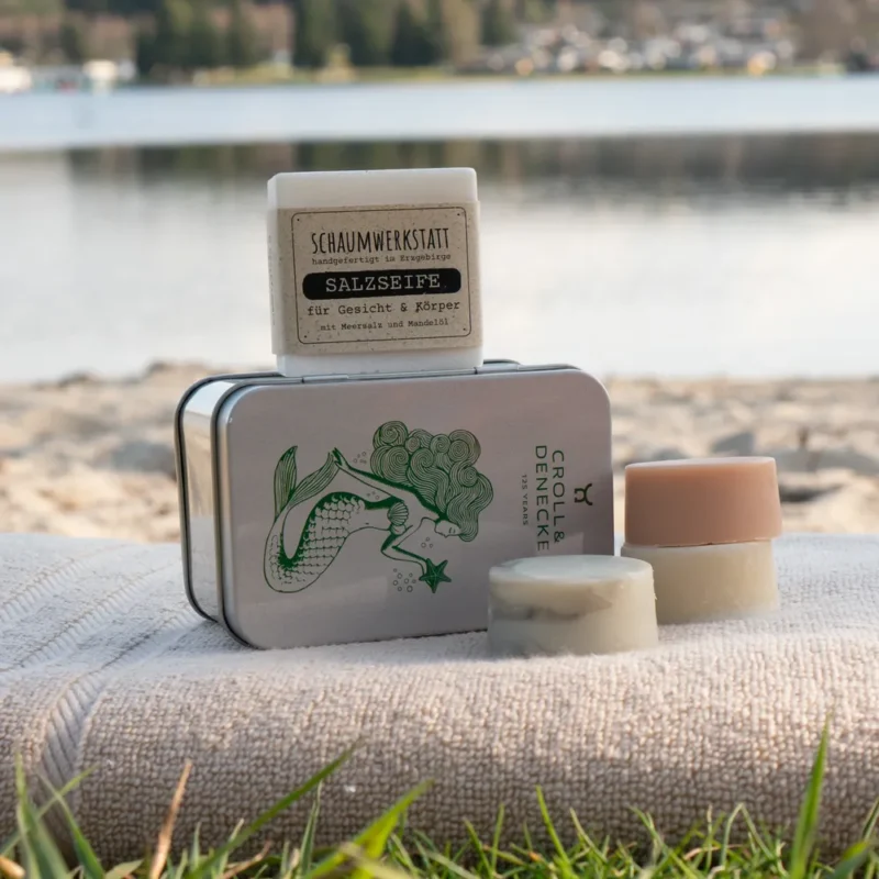 Seifendose und drei Naturseifen auf einem Handtuch arrangiert am Strand