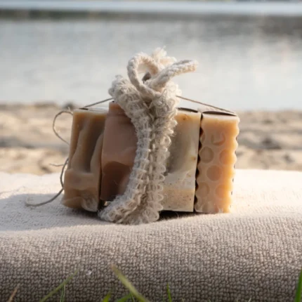 Vier Naturseifen und ein Sisalsäckchen zusammengebunden liegen auf einem Handtuch am Strand